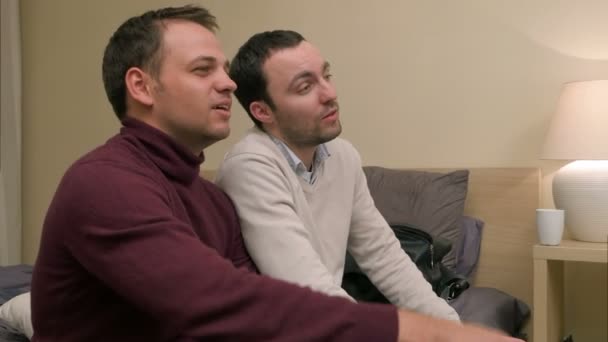 Двоє чоловіків друзів на дивані дивиться телевізор і сміється — стокове відео