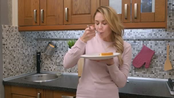 Attractive young blond woman break up the diet and eating cake in modern kitchen — Stock Video