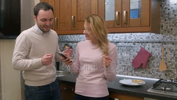 Beau couple sourit tout en dansant et en écoutant de la musique via smartphone dans la cuisine à la maison — Video