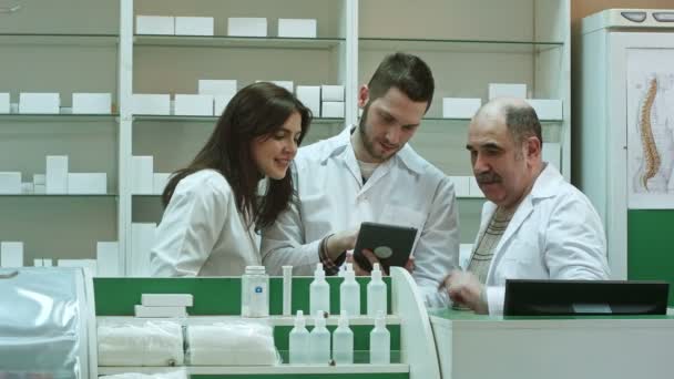 Mosolyogva csapat a gyógyszerészek, két férfi és egy nő, áll egymás mellett a gyógyszertár, egy tabletta számítógép ellenőrzése — Stock videók