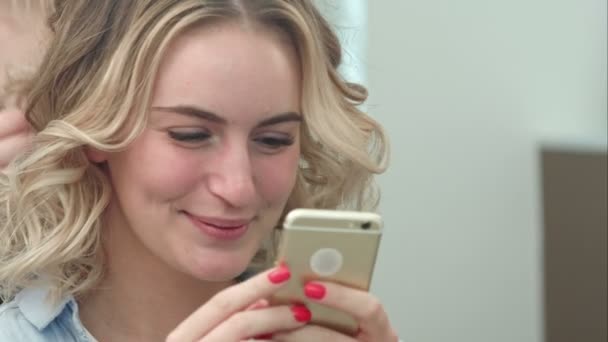 Frau frisiert sich im Salon, während sie auf ihrem Handy im Internet surft und lächelt — Stockvideo