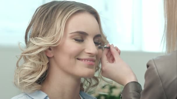 Professionelle Visagistin kämmt Wimpern des Models in weißem Raum — Stockvideo