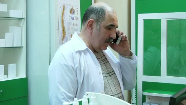 Senior pharmacist talking on mobile phone while checking prescription in pharmacy — Stock Video