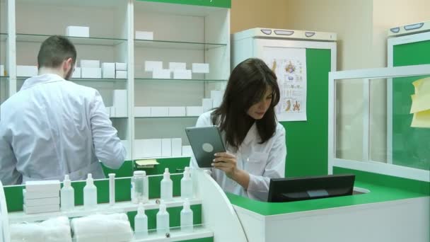 Фармацевт работает с планшетом в аптеке, держа его в руке, пока читает информацию — стоковое видео