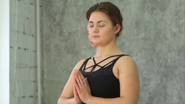 Портрет молодой красивой атлетичной девушки, практикующей йогу в помещении с закрытыми глазами и пальмами в жест намасте — стоковое видео