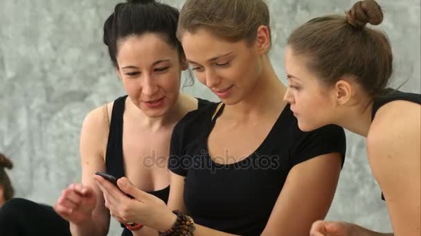 Tre unga kvinnor med smartphone och skrattar efter träningspass på yogaklass — Stockvideo