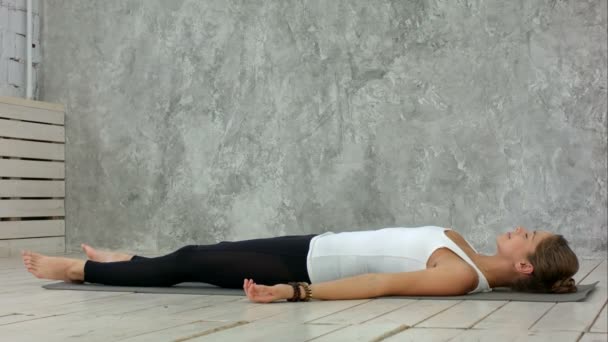 Привлекательная молодая женщина, тренирующаяся дома, занимающаяся йогой на синем коврике, лежащая в Shavasana Corpse или Dead Body Posture, отдыхающая после тренировки, медитирующая, дышащая — стоковое видео