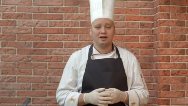 Sonriente cocinero de pie en la cocina y hablando con la cámara sobre el plato que va a preparar — Vídeos de Stock