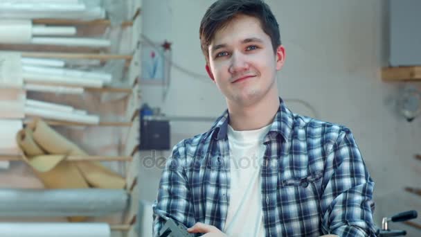 Joven trabajador alegre en un taller de taller de marco sonriendo y mirando a la cámara — Vídeo de stock