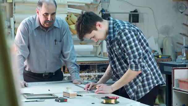 Joven aprendiz construyendo un marco detrás del escritorio en el taller de marco — Vídeos de Stock