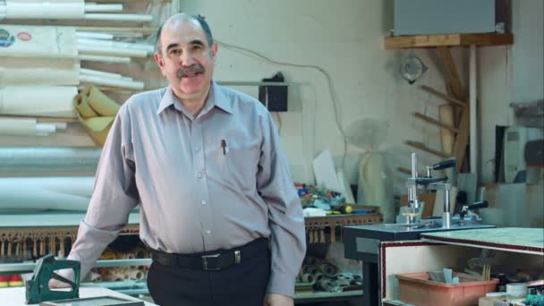 Porträt eines älteren männlichen Geschäftsinhabers hinter dem Tresen seiner Rahmenwerkstatt, stehend und im Gespräch mit einer Kamera — Stockvideo