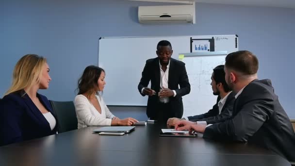 Amistoso empresario africano confiado en una reunión de gestión con un grupo de colegas multirraciales — Vídeos de Stock