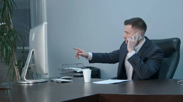 Junger kaukasischer Geschäftsmann telefoniert mit Smartphone und redet ernsthaft im Büro — Stockfoto
