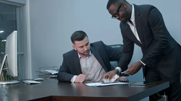 Empresários afro-americanos contando dinheiro na mesa e dando contas ao seu parceiro caucasiano, apertam as mãos positivamente — Fotografia de Stock