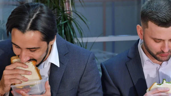 Two businessmen eating sandwich at lunch in office