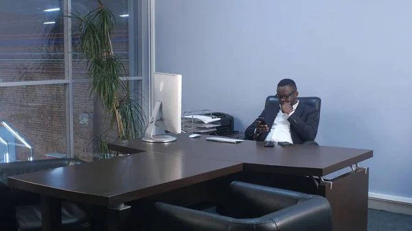 Genç afro Amerikalı işadamı smartphone, oturma içinde yazıhane ile tarama — Stok fotoğraf