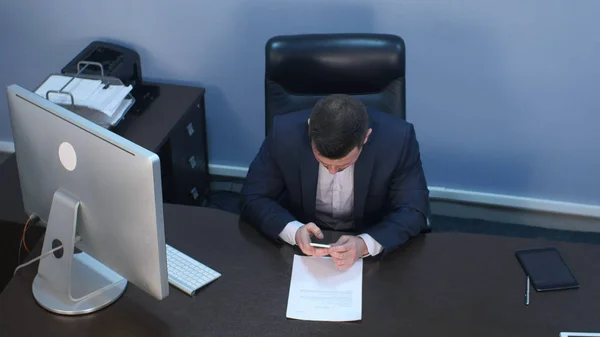 Bärtiger Geschäftsmann sitzt mit Smartphone am Schreibtisch im Büro — Stockfoto