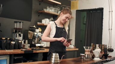 Neşeli ve içerik kadın barista kahve dükkanında hareket eden telefon, mesaj kullanarak