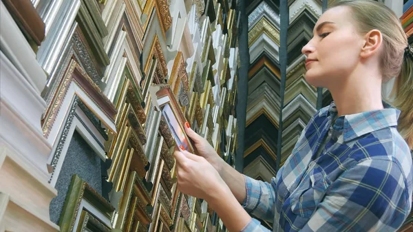 Joven cliente femenino buscando un marco en una tienda especial — Foto de Stock