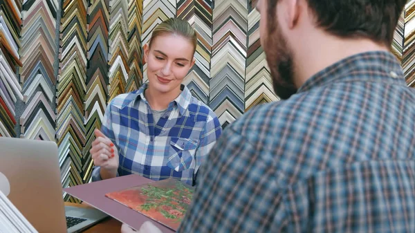 Vendedora alegre ayudando al cliente con marco y passepartout para su pintura en la tienda — Foto de Stock