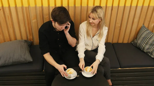 Mladý muž volání z mobilního telefonu, zatímco sedí v kavárně s přítelkyní — Stock fotografie