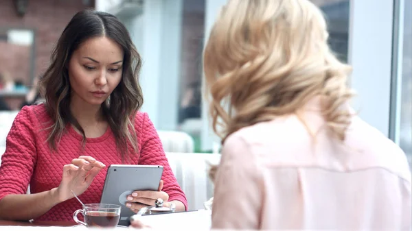 Две молодые деловые женщины сидят за столом в кафе, используя цифровой планшет — стоковое фото
