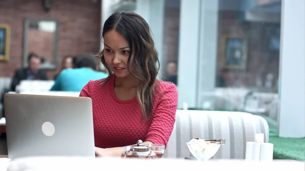 Hermosa mujer asiática soñando con algo mientras está sentado con portátil net-book en moderno bar cafetería — Foto de Stock