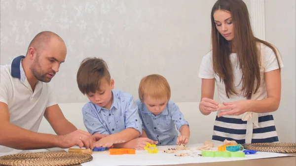 Young parents teaching their little boys how to make cookies