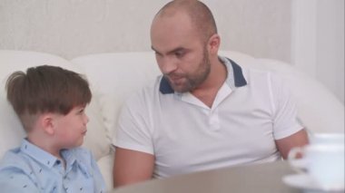 Baba oğul evdeki kanepede dijital tablet kullanıyorlar.