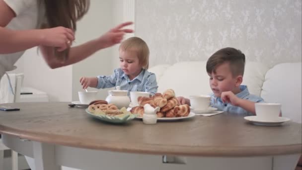 Двоє маленьких хлопчиків п'ють чай з тістечком за столом — стокове відео