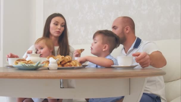 Счастливая молодая семья наслаждается чаем со сладостями в ресторане или кафе или дома — стоковое видео