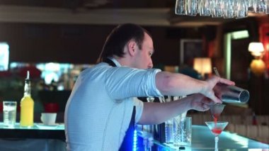 Karışık likörü kokteyl süzgeç aracılığıyla hazırlanan cam içine dökme ve bir müşteri ile konuşurken barmen yan görünümü