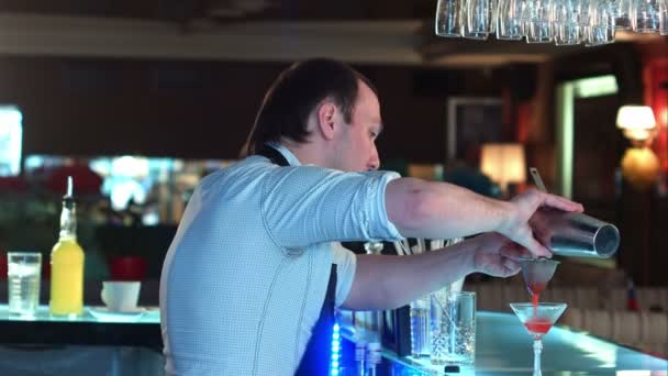 Seitenansicht des Barkeepers, der gemischten Likör durch ein Cocktailsieb in ein vorbereitetes Glas gießt und mit einem Kunden spricht — Stockvideo