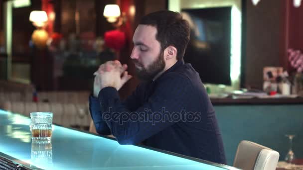 Веселый привлекательный молодой человек пьет в баре и смотрит в камеру улыбаясь — стоковое видео