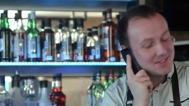 Feliz barman en delantal llamando en el teléfono inteligente en el bar — Vídeo de stock