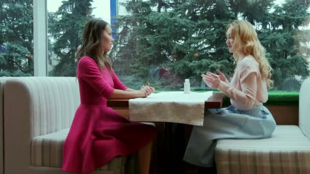 Két mosolygó gyönyörű fiatal nő beszél az asztalnál, kávézó — Stock videók