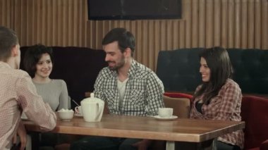 Bir grup genç bir kafede oturuyor, konuşuyor ve eğleniyorlar.