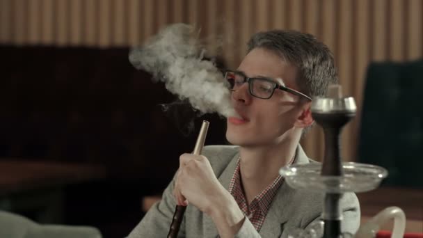 Un joven fuma narguile en la cafetería — Vídeo de stock
