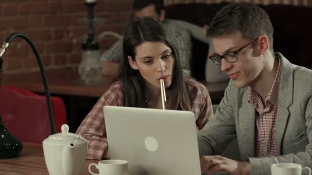 Young couple at cafe looking at laptop and smoking hookah — Stock Video