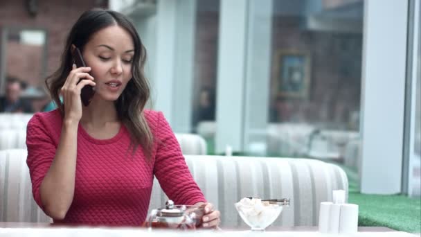 Joven encantadora mujer llamando con teléfono celular mientras está sentada sola en la cafetería — Vídeo de stock