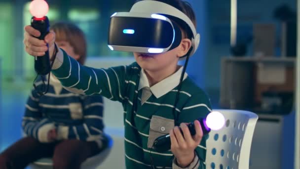 Мальчик в гарнитуре vr играет в виртуальную реальность с контроллерами, в то время как другой мальчик ждет своей очереди — стоковое видео