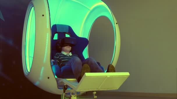Маленький мальчик наслаждается виртуальной реальностью в движущемся интерактивном кресле — стоковое видео