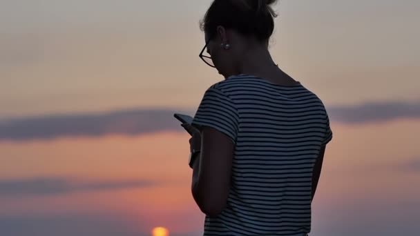 Kvinna textning på smartphone på stranden under solnedgången — Stockvideo