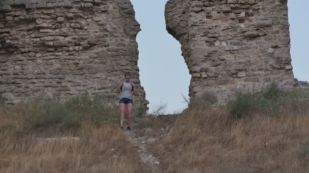 Улыбающаяся туристка идет по тропинке и смотрит на руины — стоковое видео