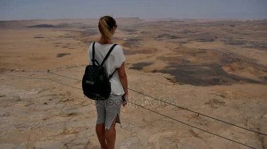 Uçurum kenarında duran ve çöl manzarayı sırt çantası olan kadın