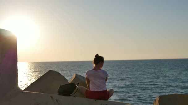 Sogno giovane donna seduta sulle rocce godendo il mare al tramonto — Video Stock