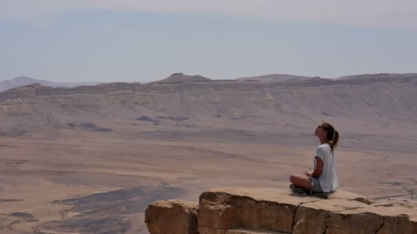 선글라스 절벽 가장자리에 앉아 및 사막 주변에 젊은 여자 — 비디오