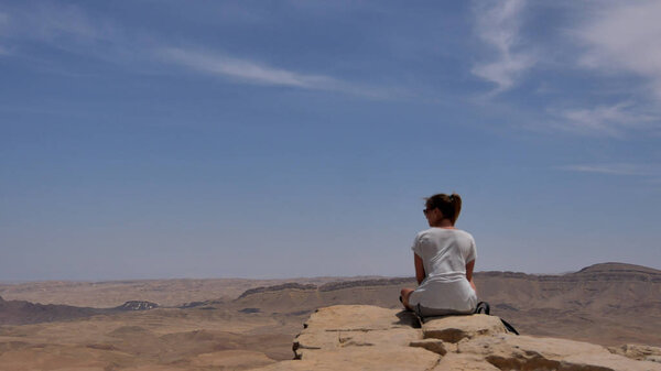 Young woman sitting on cliffs edge and looking at the desert