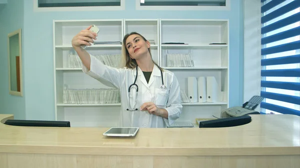 Улыбающаяся медицинская работница делает селфи с телефоном на ресепшене — стоковое фото