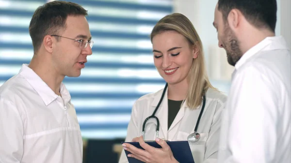 Два врача-мужчины обсуждают это, улыбаясь медсестре, делая заметки в ее блокноте — стоковое фото